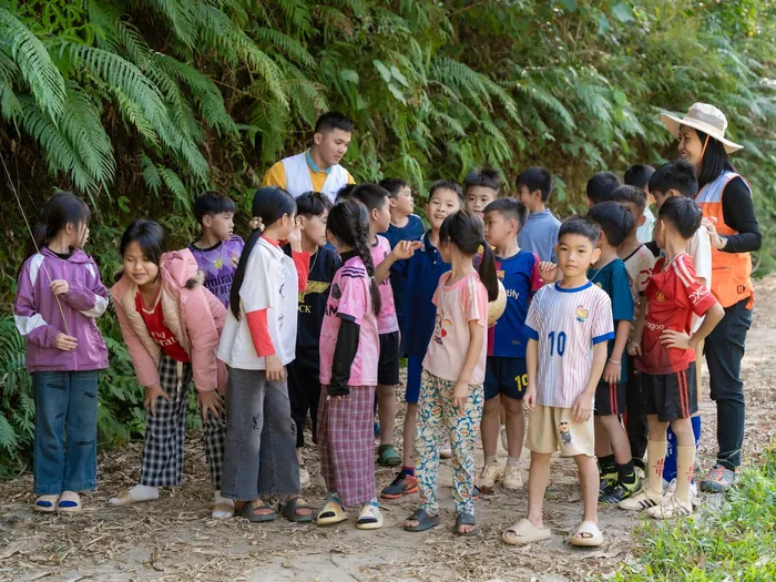 A group of children gathered on a shaded woodland trail with two adult guides during an outdoor nature activity.